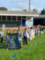 This image links to the Saint Nicholas Catholic School In-School connections page. It depicts kindergarteners leading a Marian procession to our Mary Grotto in May