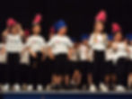 The photograph links to the Saint Nicholas Catholic School Actitvities and Extended Care page. The image depicts young elementary school students dancing and singing in  a Young Performers performance on stage. Our young performers open for the spring musical.