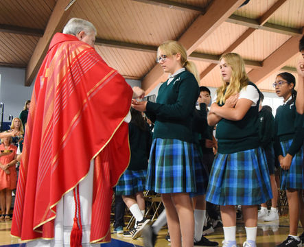 A priest gives a middle school student Communion at a Mass at Saint Nicholas Catholic School