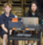 A link to the Saint Nicholas Catholic School High School Acceptances Page. The image shows a boy and a girl sitting at two computers, helping run the audio-visual equiptment at an assembly.