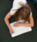 A link to the Saint Nicholas Catholic School Academics Page. The photo shows a girl laying on the floor writing an essay in her compostion notebook.